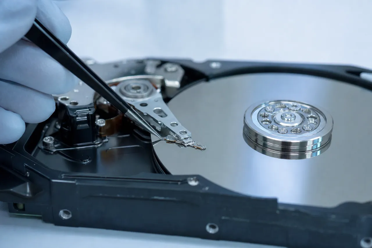 Technician using tweezers to lift a read/write head off the platter of an opened hard drive during recovery at MDRepairs